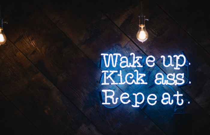 Esta imagem mostra uma frase de néon inspiradora que representa a rotina motivacional de muitos empreendedores: acordar com propósito, agir com confiança e repetir com consistência. Perfeita para ilustrar os componentes da motivação no dia a dia.